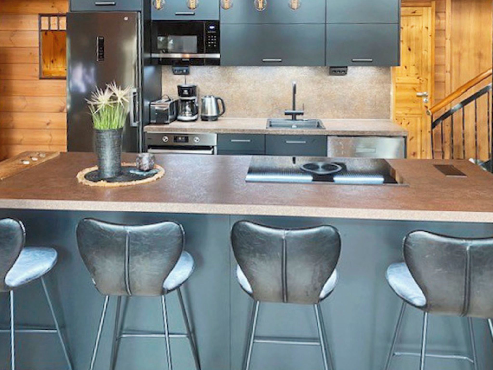 Een keuken met een centraal eiland, barstoelen en moderne apparaten.
