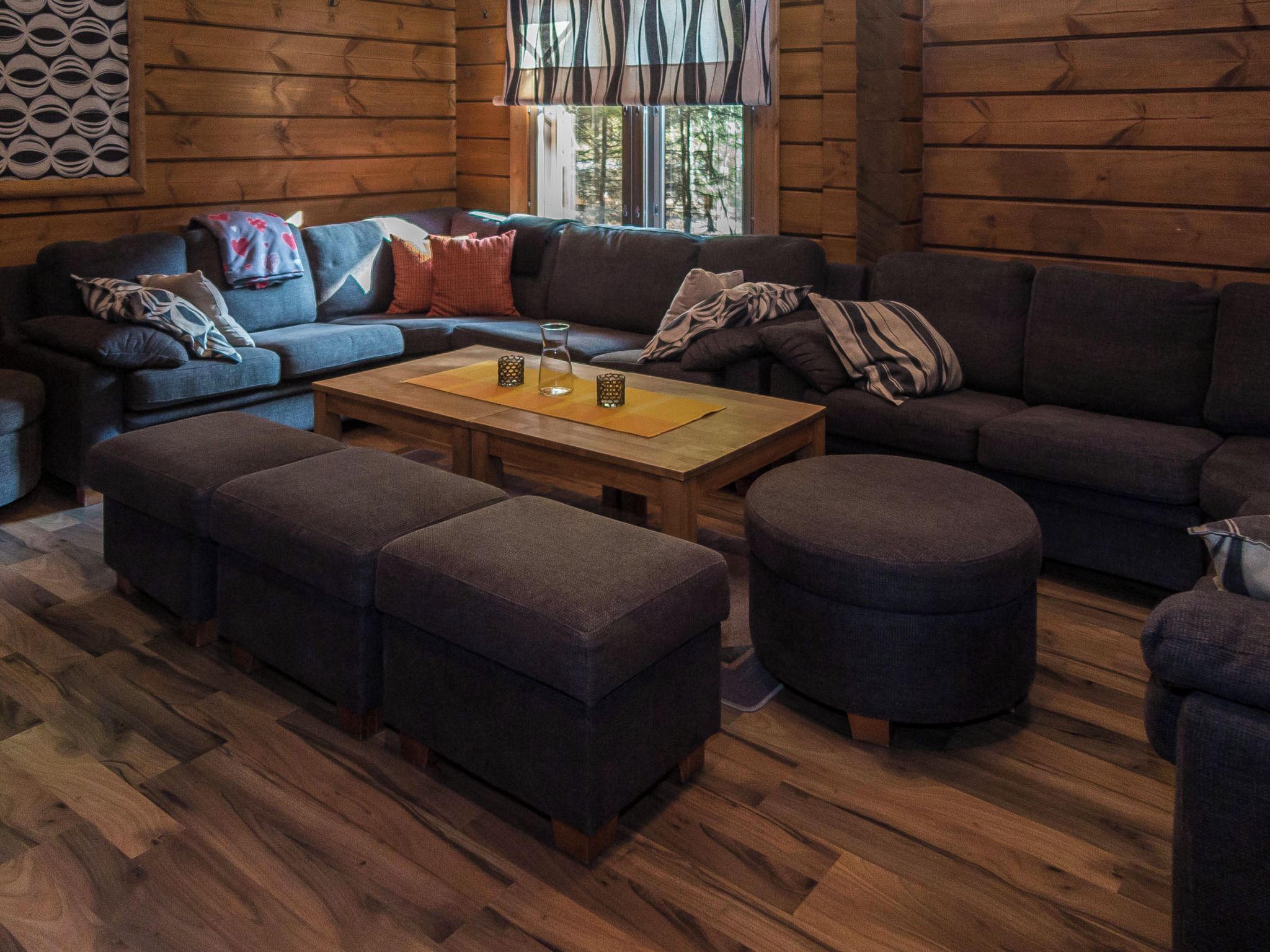 Un intérieur chaleureux de chalet en bois, avec un canapé d’angle, des poufs et une table basse en bois.