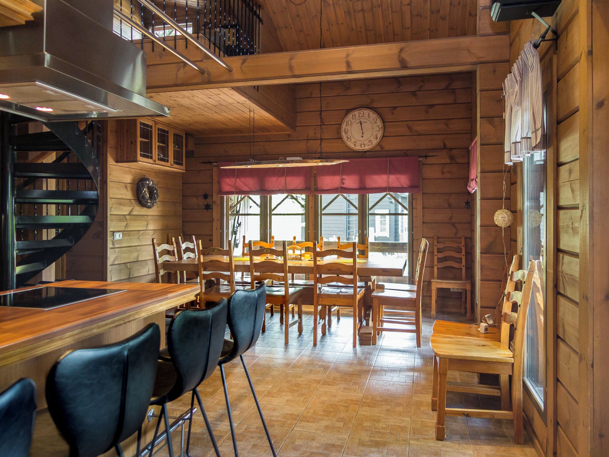 A rustic interior with a wooden bar, multiple chairs, a dining table, and a clock on the wall.
