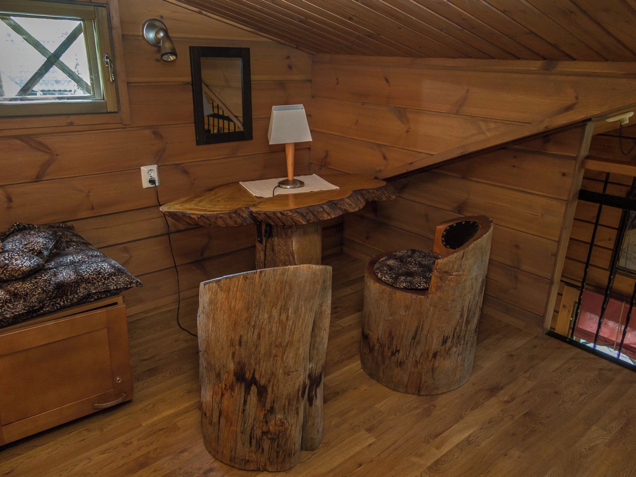 Interior acogedor de una cabaña con un banco de madera, una mesita con una lámpara y un sillón.