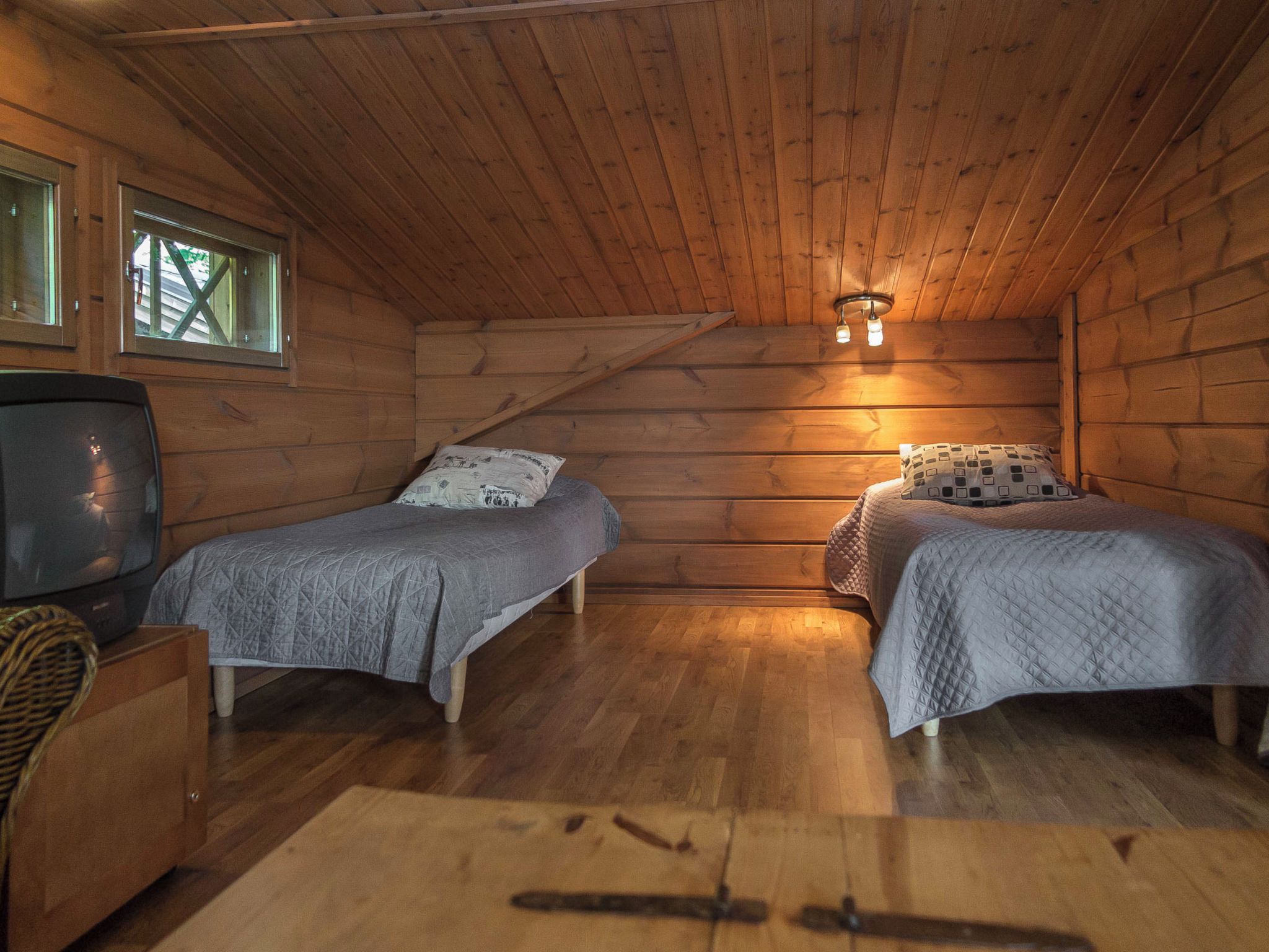 Een gezellig vakantiehuisje met twee bedden, een televisie en een houten plafond.