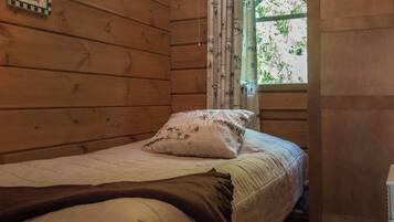 Una cama individual con un cojín blanco y estampado, una manta marrón y una ventana con cortinas verdes.