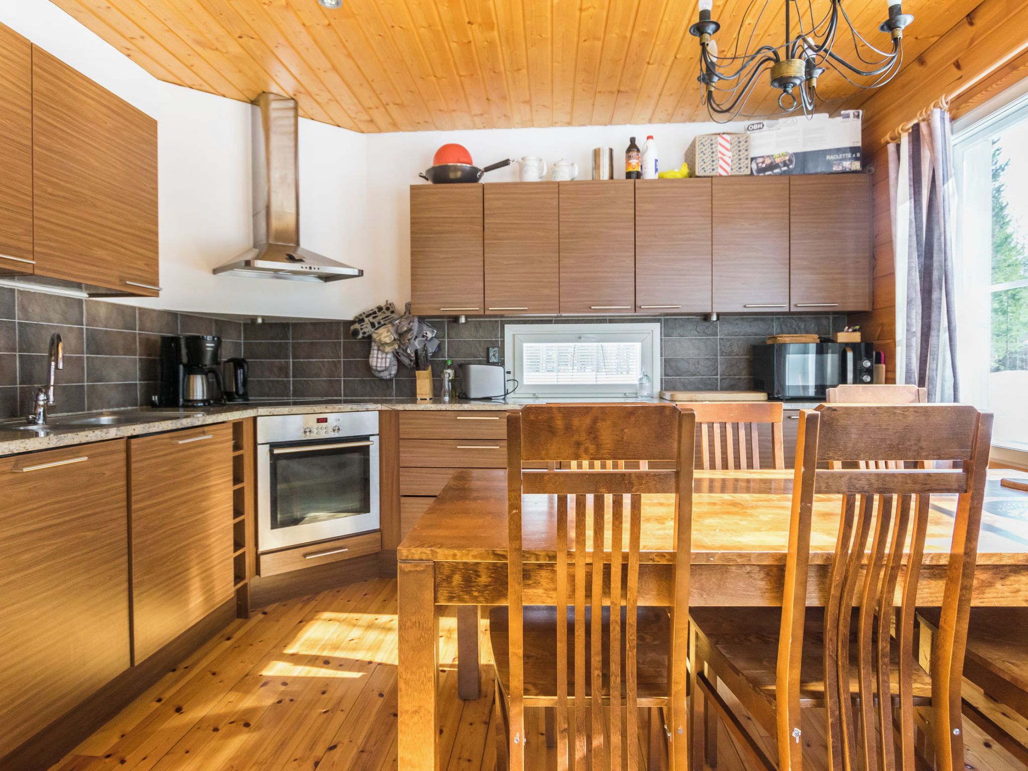 Een moderne keuken met houten kastjes, een ingebouwde oven en een eettafel met stoelen.