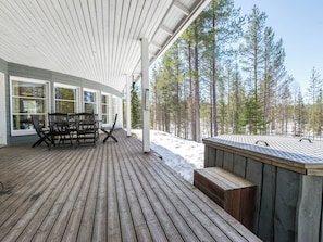 A wooden deck with a hot tub, outdoor seating, and a view of a forest. - Luppoaika by Interhome (Kuusamo)