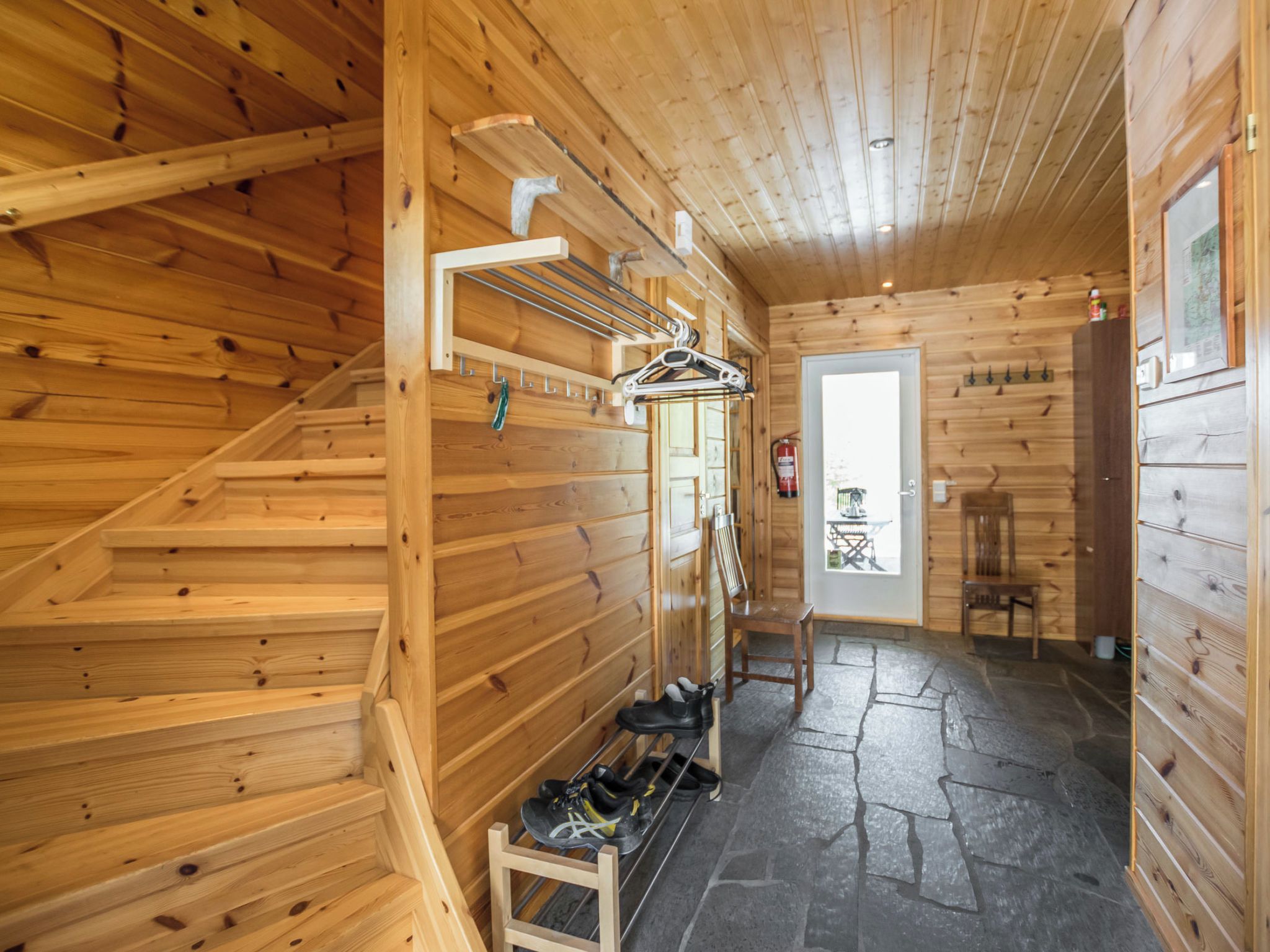 A wooden interior with a staircase, a shoe rack, and a door leading to another room.
