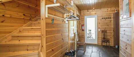 Een houten interieur met een trap, een schoenenrek en een deur naar een andere kamer.