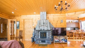 Een gezellig chaletinterieur met een stenen open haard, houten wanden, een eethoek en een televisie.