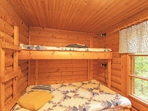 A bunk bed in a wooden cabin room with a window and a patterned curtain.