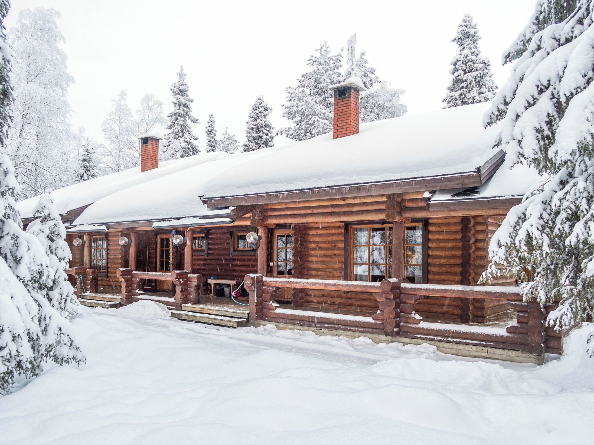 A log cabin with a wooden porch and a chimney, surrounded by snow-covered trees.