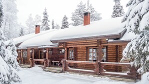 Een blokhut met een houten veranda en schoorsteen, omringd door met sneeuw bedekte bomen.