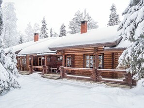 Een blokhut met een houten veranda en schoorsteen, omringd door met sneeuw bedekte bomen.