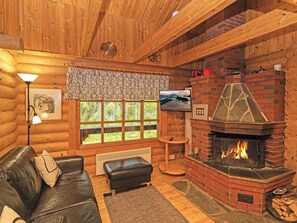 A cozy log cabin interior with a fireplace, leather sofa, and a television.