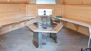 Een houten interieur met een centrale metalen kachel, banken en een raam.