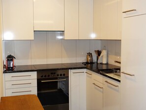 Eine moderne Küche mit weißen Schränken, einer schwarzen Arbeitsplatte und Edelstahlgeräten, darunter ein Backofen und eine Kaffeemaschine.