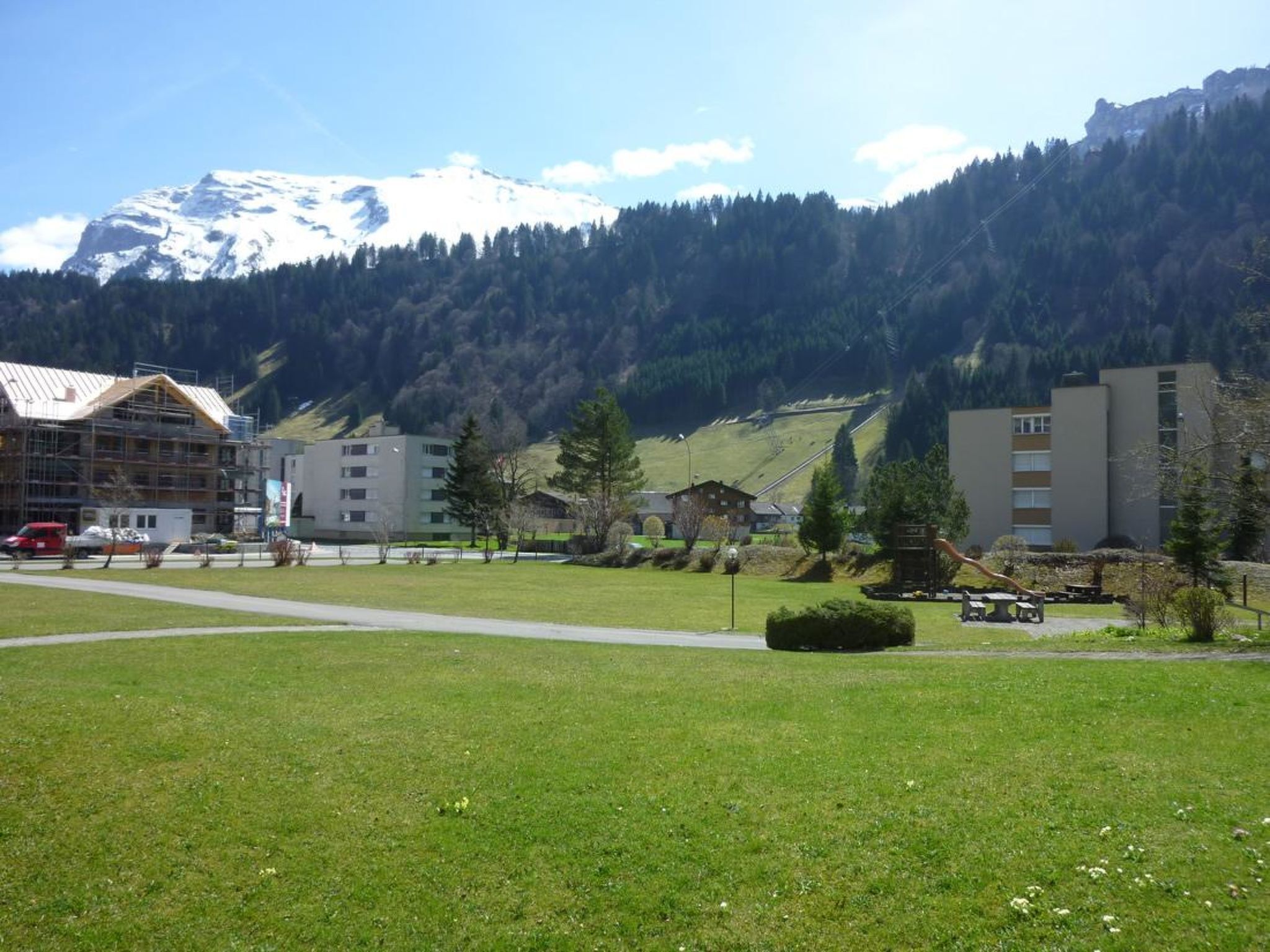 A grassy area with buildings, a mountain, and a clear sky.