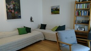 Un salon comprenant un canapé, un fauteuil, une bibliothèque et deux tableaux accrochés au mur.