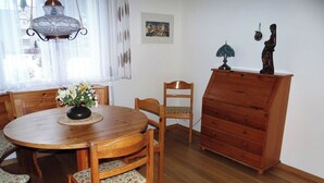 Un coin repas comprenant une table en bois, des chaises, un vase de fleurs, une commode en bois et une lampe suspendue.