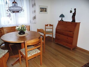 Ein Essbereich mit Holztisch, Stühlen, einem Blumenstrauß, einer Holzkommode und einer Hängelampe.