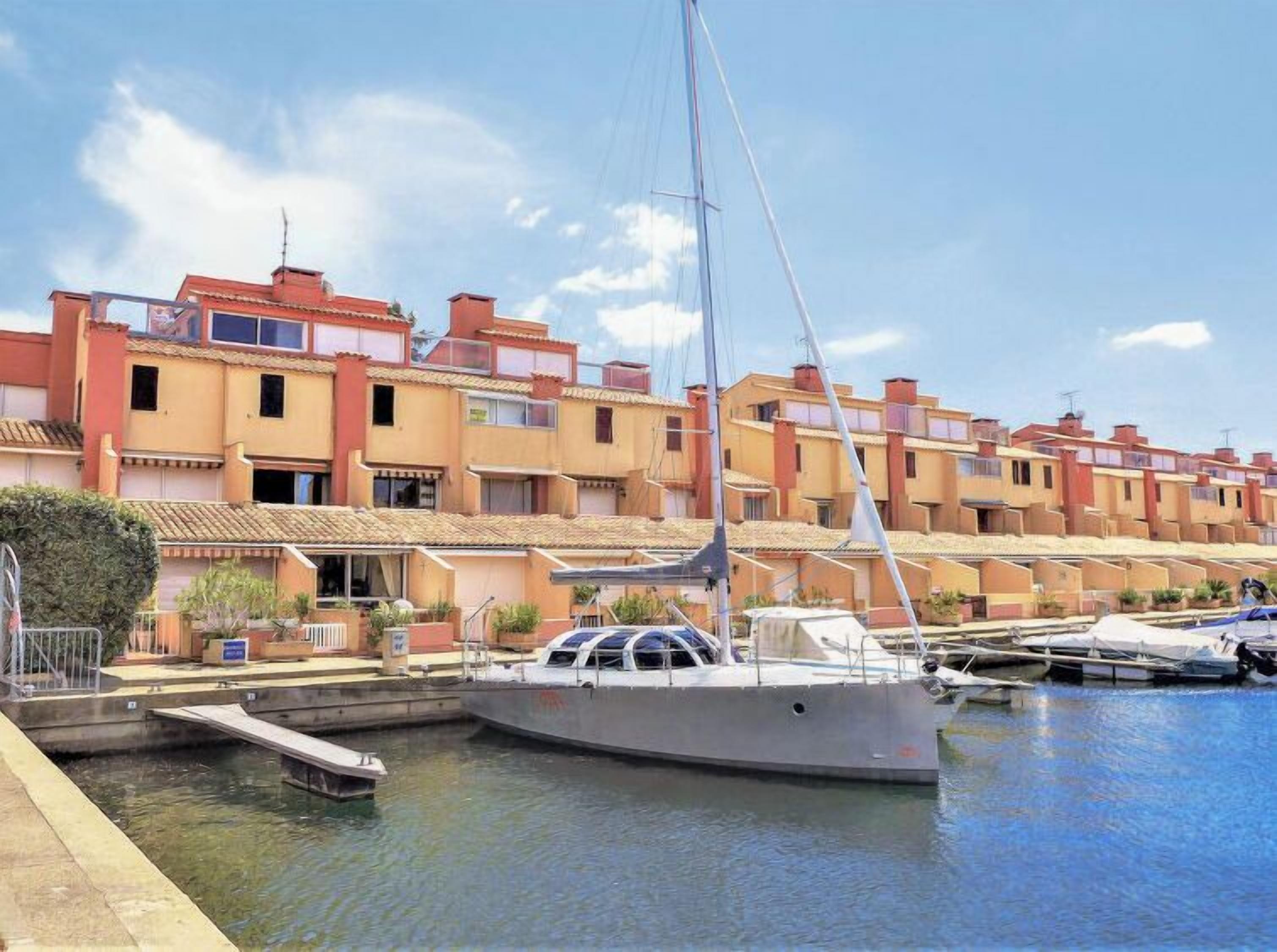 A marina with a sailboat docked, surrounded by multi-story buildings with balconies.