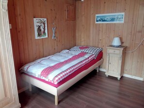 Una cama individual con una colcha estampada, una mesita de noche pequeña con una lámpara, y un cuadro en la pared.