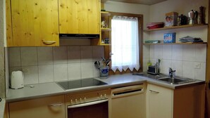 A compact kitchen with wooden cabinets, a built-in oven, a sink, and a window with a curtain. - Steinacher 7 Appartement/Fewo 4-Bettwohnung by Interhome (Engelberg)
