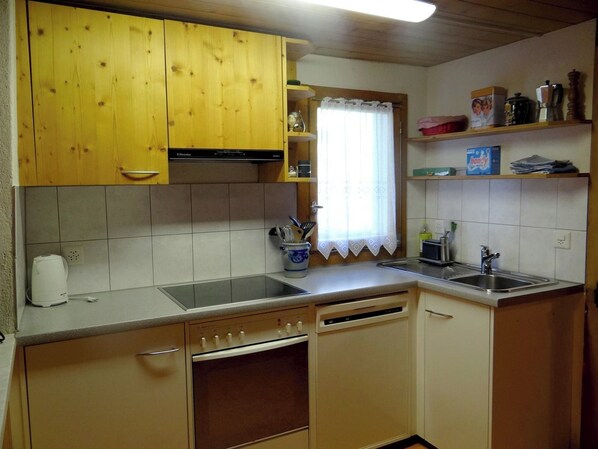 A compact kitchen with wooden cabinets, a built-in oven, a sink, and a window with a curtain.