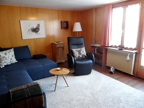 Una sala de estar con un sofá azul, un sillón negro, una mesita de madera y un radiador.