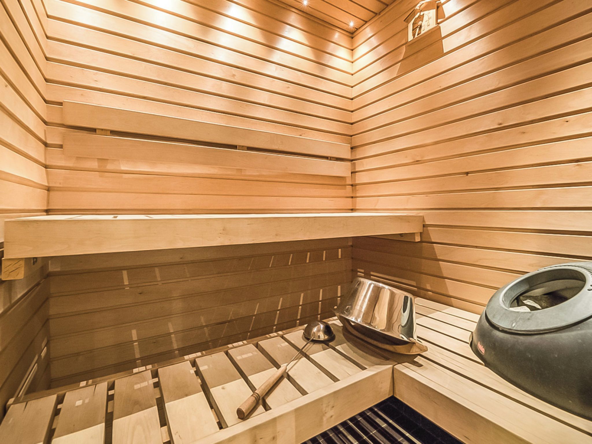 Een sauna met houten latten, een metalen bank en een grote zwarte bak.