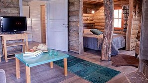 A log cabin interior with a television on a wooden table, a bed with a blue blanket, and a rustic wooden floor. - Peltotupa by Interhome (Asikkala)