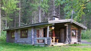 A rustic log cabin with a porch, a chimney, and a small table with a chair. - Peltotupa by Interhome (Asikkala)