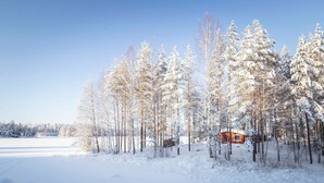 Une cabane entourée d’arbres couverts de neige, dans un paysage hivernal.