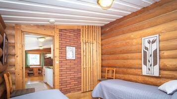 Ein Ferienhausinnenraum mit zwei Betten, einer Holzwand, einer Ziegelwand und einer Deckenleuchte.