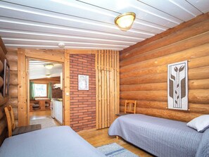 Ein Ferienhausinnenraum mit zwei Betten, einer Holzwand, einer Ziegelwand und einer Deckenleuchte.