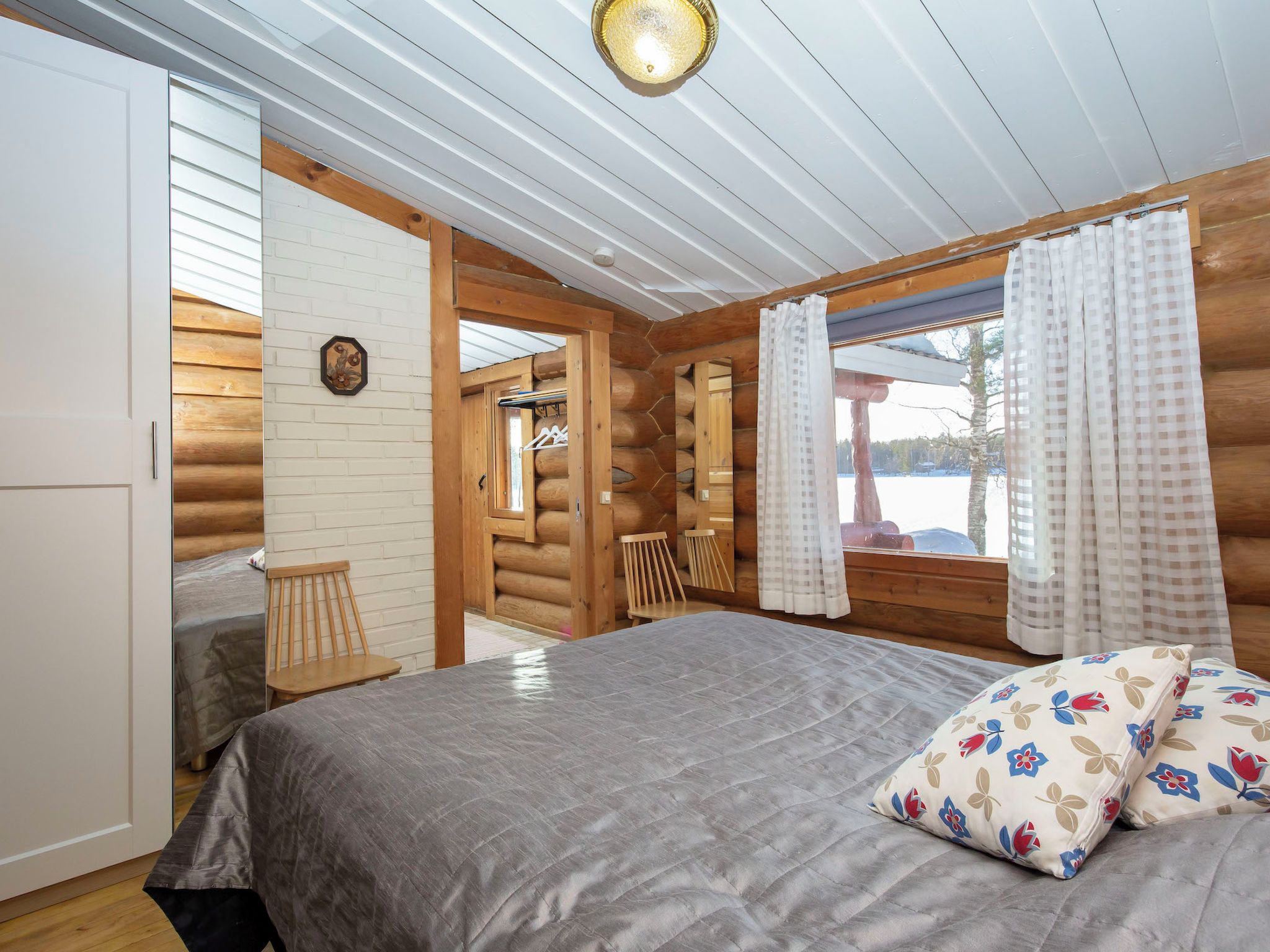 Une chambre à coucher dans un chalet en rondins, avec un lit, une chaise, une armoire en bois et une fenêtre avec des rideaux.