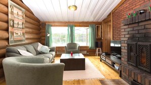L’intérieur d’une cabane en rondins, avec un canapé, un fauteuil, une cheminée et un tableau accroché au mur.