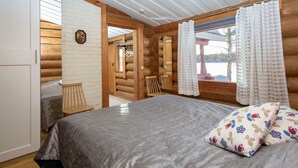 Une chambre dans un chalet en rondins, avec un lit, des murs en bois, une fenêtre avec des rideaux et un luminaire au plafond.