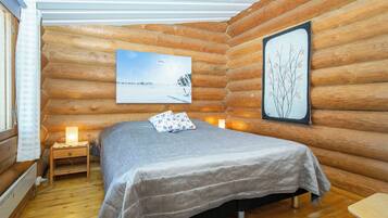 Une chambre à coucher dans un chalet en rondins, avec un lit, des lampes de chevet, un tableau encadré et une fenêtre avec des rideaux.