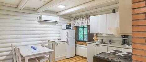 A compact kitchen with white cabinetry, a dining table with chairs, a microwave, a refrigerator, and a coffee maker.