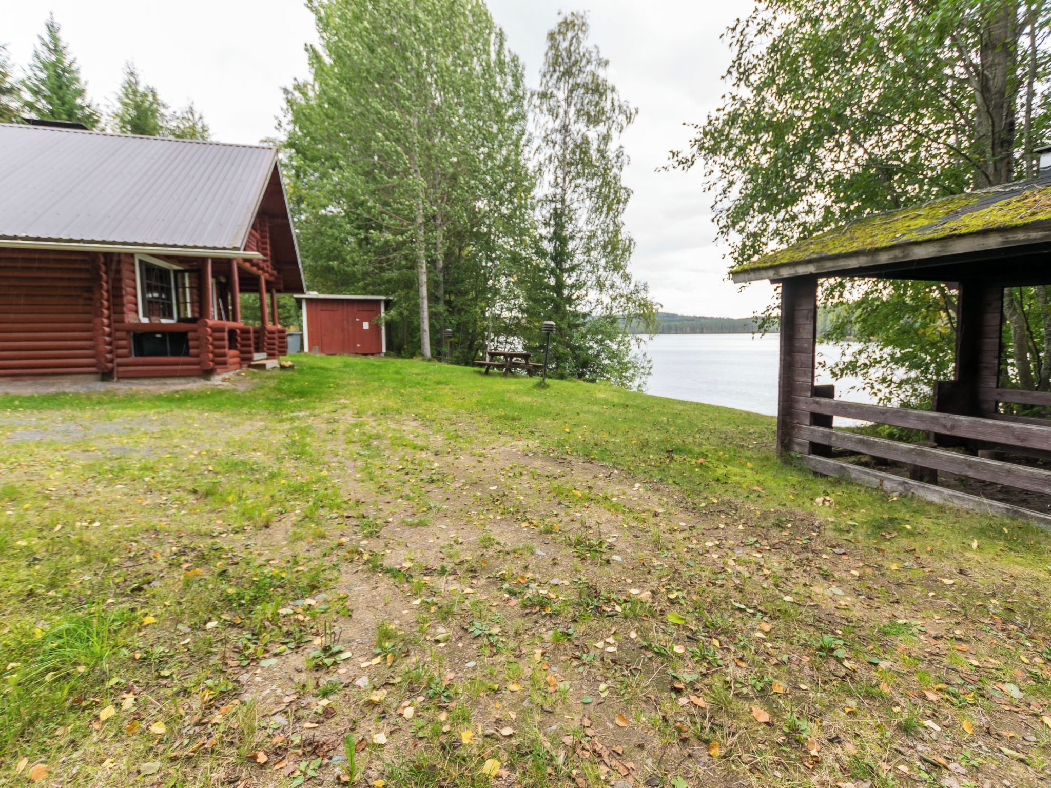 Un chalet rustique doté d’une véranda et d’un petit abri de jardin, d’une table de pique-nique et d’une terrasse en bois offrant une vue sur un lac.