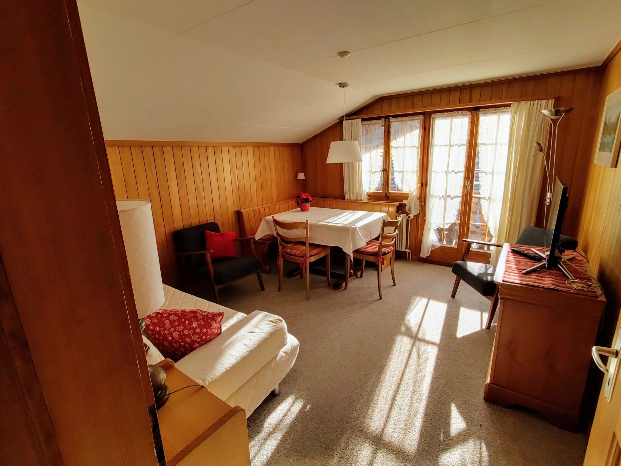 Una habitación acogedora con cama, un escritorio con computadora, una mesa de comedor con sillas y una ventana con cortinas.