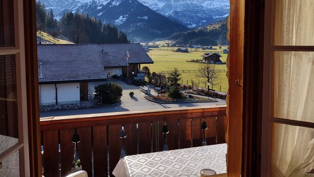 A balcony with a view of a mountain landscape, a building with a sloped roof, and a small garden area. - Bärnermutz # 2 by Interhome (Lenk)
