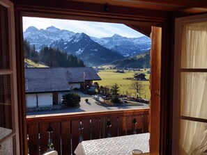 Ein Balkon mit Blick auf eine Berglandschaft, ein Gebäude mit Satteldach und eine kleine Gartenanlage.
