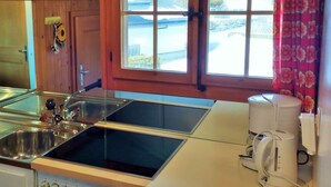 A kitchen with a double sink, a coffee machine, and a view of a building through a window. - Bärnermutz # 2 by Interhome (Lenk)