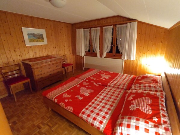 Ein Schlafzimmer mit Holzwänden, einem Bett, einem Schminktisch, einem Sessel und einem Fenster mit Vorhängen.