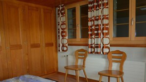 Ein Schlafzimmer mit einem Bett, zwei Holzstühlen, einem fenster mit Vorhängen und Holzschränken.