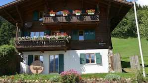 Eine zweistöckige Holzhütte mit Balkonen, geschmückt mit Blumen, einer Schweizer Flagge und einem Schild mit der Aufschrift 'Belfort'.