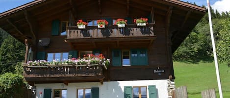 En tvåvånings chalet i trä med balkonger som är dekorerade med blommor, en schweizisk flagga och en skylt som visar att det är "Belfort".
