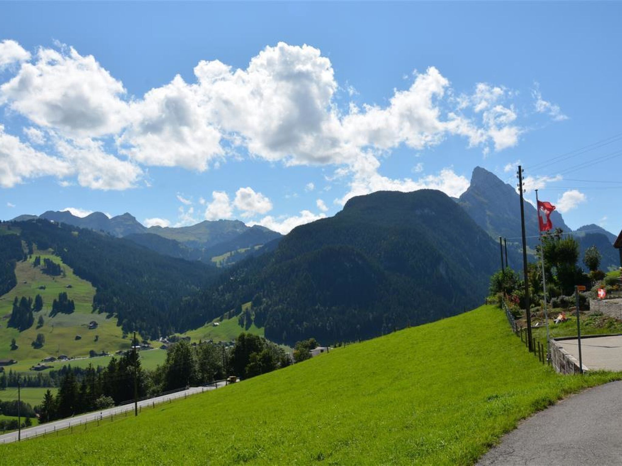 A mountain landscape with a clear sky, a road, and a flagpole with a flag.