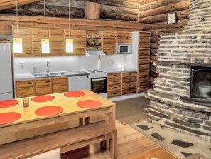A rustic kitchen with wooden cabinets, a stone wall, and a dining area with a wooden table and red placemats.