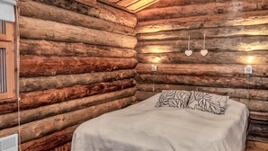 A log cabin bedroom with a bed, a heater, and a window.